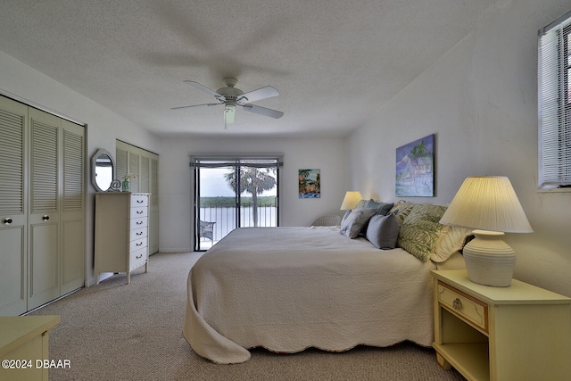 carpeted bedroom featuring access to outside, a water view, a textured ceiling, and ceiling fan