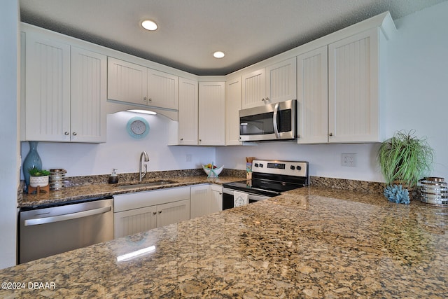 kitchen with dark stone countertops, appliances with stainless steel finishes, sink, and white cabinets