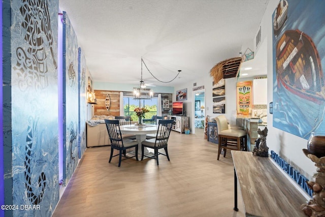 dining area with light hardwood / wood-style floors, a textured ceiling, and an inviting chandelier