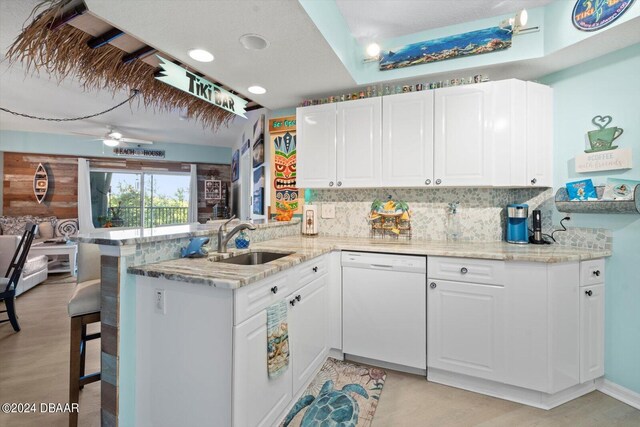 kitchen with sink, a breakfast bar, kitchen peninsula, white cabinets, and dishwasher