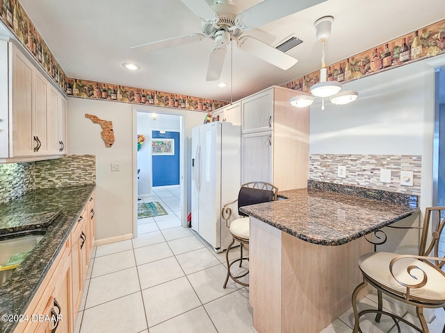 kitchen with a kitchen bar, kitchen peninsula, pendant lighting, dark stone countertops, and white fridge with ice dispenser