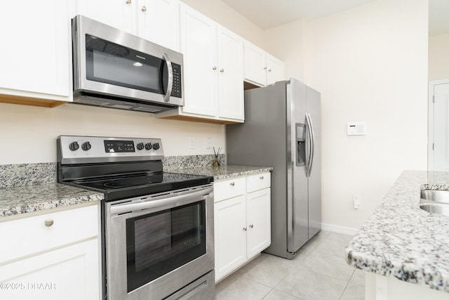 kitchen featuring appliances with stainless steel finishes, white cabinets, light tile patterned floors, light stone countertops, and baseboards
