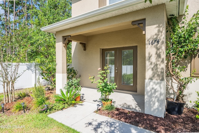 entrance to property featuring stucco siding, fence, and french doors