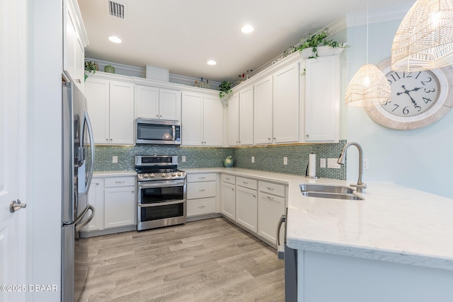 kitchen featuring sink, light hardwood / wood-style flooring, white cabinetry, stainless steel appliances, and decorative light fixtures