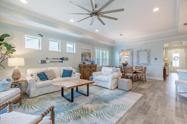 living room featuring crown molding, a healthy amount of sunlight, a tray ceiling, and light hardwood / wood-style floors