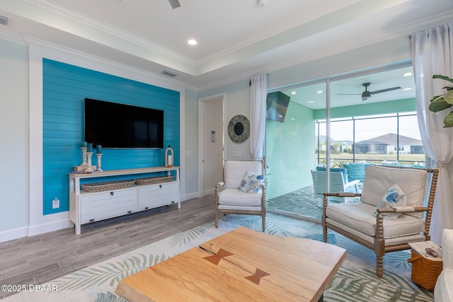 living room with crown molding, a tray ceiling, ceiling fan, and light hardwood / wood-style flooring