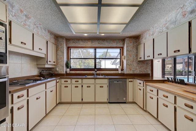 kitchen with wallpapered walls, a sink, cooktop, a textured ceiling, and dishwasher