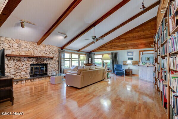 living area featuring beam ceiling, a stone fireplace, high vaulted ceiling, and wood finished floors