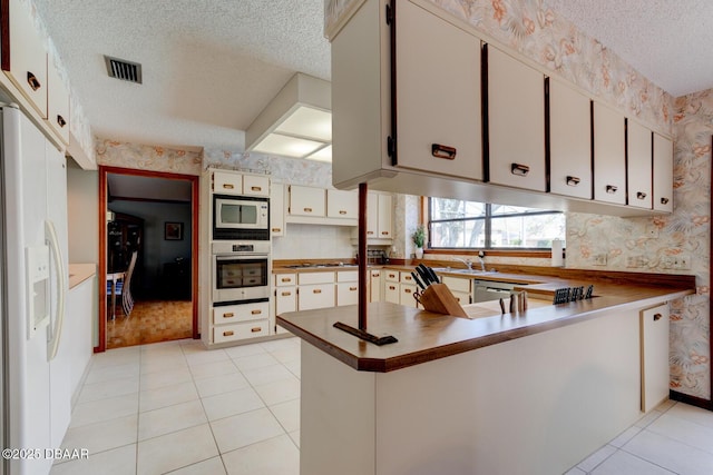 kitchen featuring visible vents, a textured ceiling, appliances with stainless steel finishes, a peninsula, and wallpapered walls