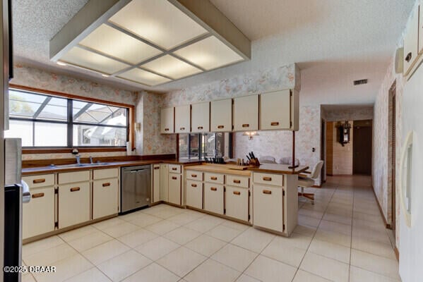 kitchen featuring wallpapered walls, a peninsula, a sink, cream cabinetry, and stainless steel dishwasher