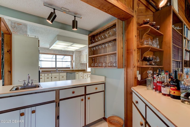 kitchen with stainless steel dishwasher, open shelves, a textured ceiling, and a sink