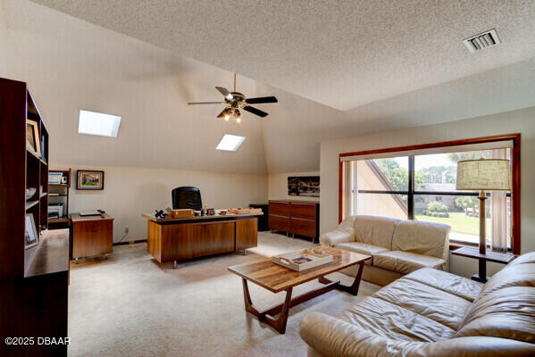 living area featuring visible vents, lofted ceiling with skylight, light colored carpet, a textured ceiling, and a ceiling fan