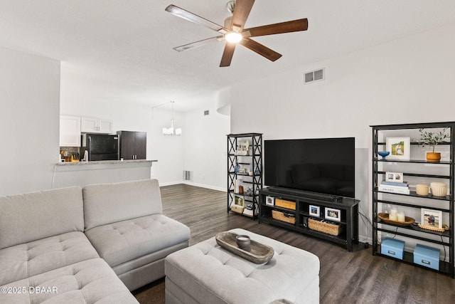 living room with dark wood-type flooring, visible vents, baseboards, and ceiling fan with notable chandelier