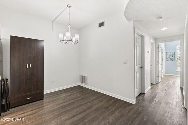 unfurnished dining area with dark wood-style floors, baseboards, visible vents, and an inviting chandelier