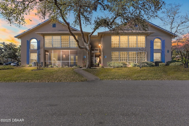 traditional-style home featuring a sunroom, stucco siding, a yard, and stairs