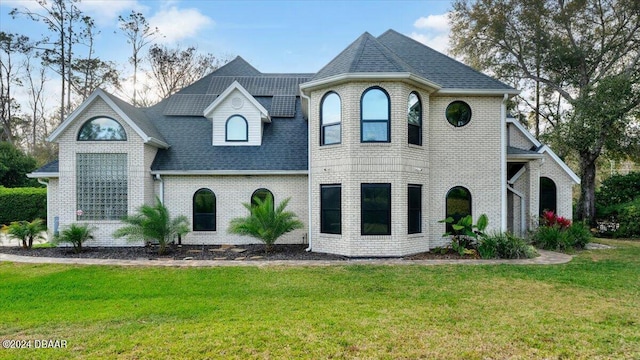 view of front of home featuring roof with shingles, brick siding, and a front lawn