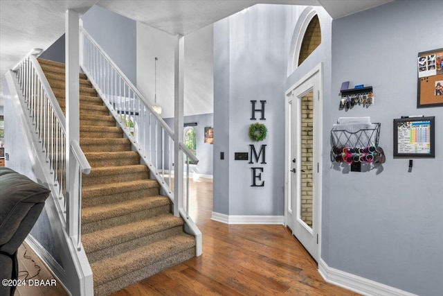 foyer featuring stairs, baseboards, a high ceiling, and wood finished floors