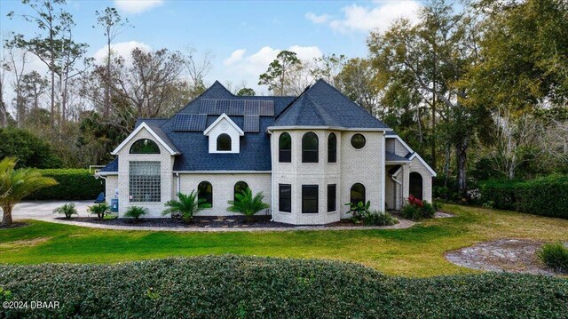 view of front of property with roof with shingles, roof mounted solar panels, a front lawn, and brick siding