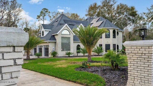 french country home with a shingled roof, a front yard, and brick siding