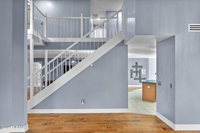 stairs with baseboards, visible vents, a high ceiling, and wood finished floors