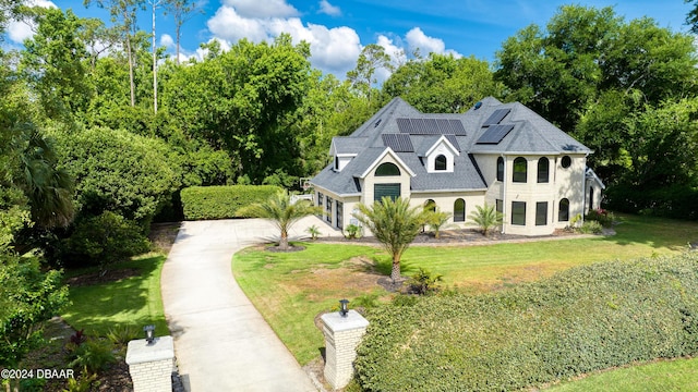 view of front of property with driveway, roof with shingles, roof mounted solar panels, and a front yard