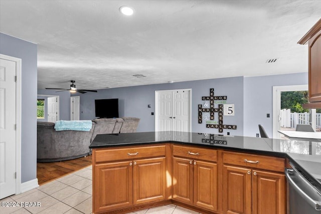 kitchen with brown cabinets, dark countertops, light tile patterned flooring, and a peninsula