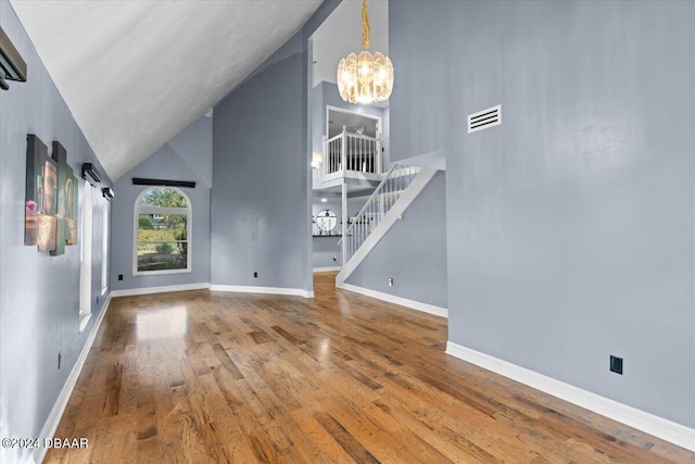 unfurnished living room with visible vents, hardwood / wood-style floors, a chandelier, baseboards, and stairs