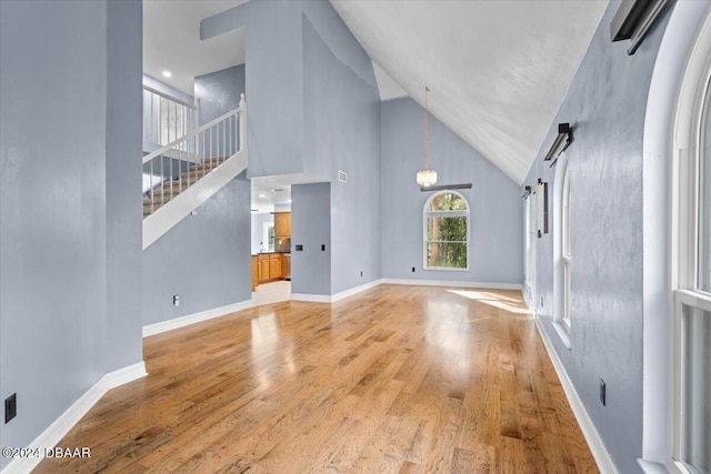 unfurnished living room with light wood-style floors, a high ceiling, and baseboards