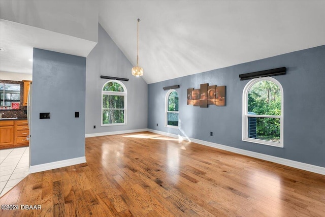 interior space featuring light wood-style floors, baseboards, and high vaulted ceiling