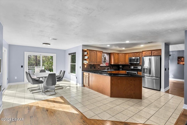 kitchen with light tile patterned flooring, stainless steel appliances, a peninsula, decorative backsplash, and dark countertops