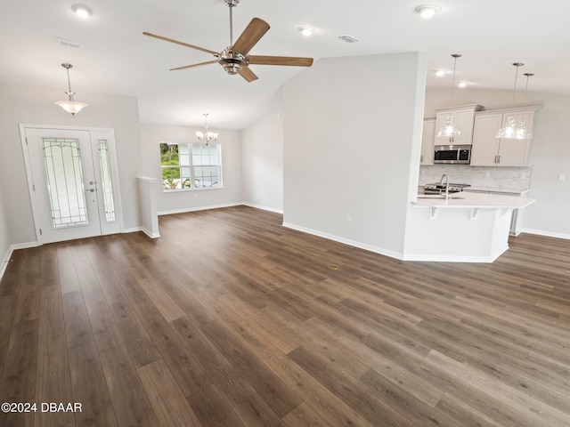 unfurnished living room with ceiling fan with notable chandelier, lofted ceiling, dark wood-type flooring, and sink