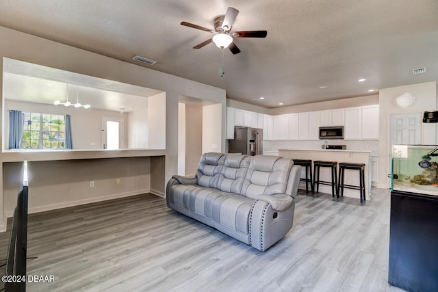 living room with a textured ceiling, ceiling fan, and light hardwood / wood-style flooring