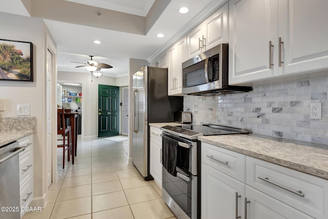 kitchen with crown molding, ceiling fan, appliances with stainless steel finishes, white cabinetry, and light tile patterned flooring