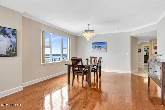 dining room featuring light wood-type flooring, a water view, a notable chandelier, and ornamental molding