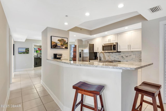 kitchen featuring light stone countertops, white cabinets, kitchen peninsula, a breakfast bar, and stainless steel appliances