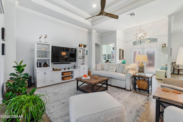 living room with crown molding, ceiling fan with notable chandelier, light hardwood / wood-style floors, and a raised ceiling