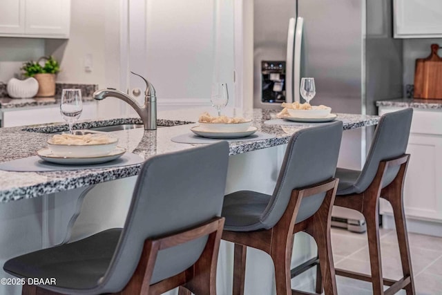 kitchen with white cabinetry, light tile patterned floors, stainless steel fridge, and light stone countertops