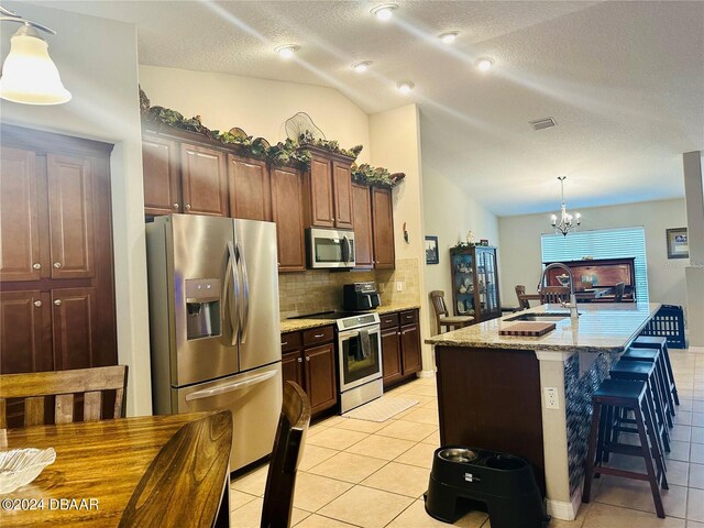 kitchen featuring stainless steel appliances, lofted ceiling, hanging light fixtures, sink, and a kitchen island with sink