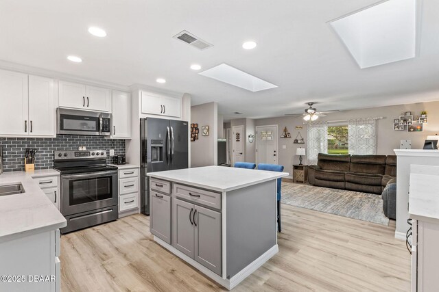 1317 Dexter Dr W, Port Orange, FL 32129 - kitchen with stainless steel appliances, a skylight, light wood-style flooring, white cabinetry, and decorative backsplash