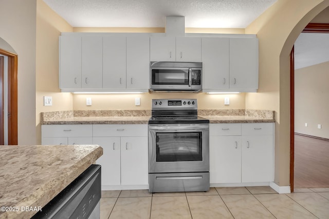 kitchen with white cabinets, light tile patterned floors, stainless steel appliances, and a textured ceiling