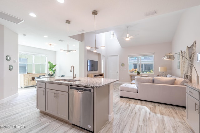 kitchen featuring decorative light fixtures, light stone countertops, sink, dishwasher, and a kitchen island with sink