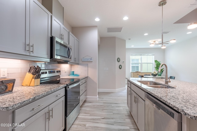 kitchen featuring light stone counters, stainless steel appliances, light wood-type flooring, hanging light fixtures, and sink