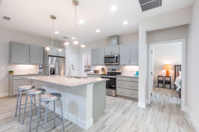 kitchen with stainless steel appliances, hanging light fixtures, sink, an island with sink, and light stone countertops