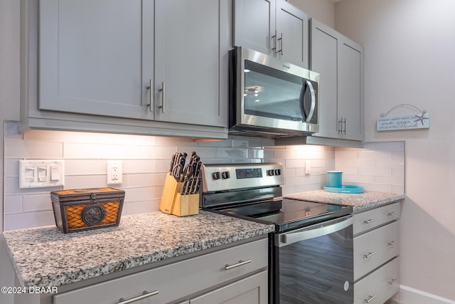 kitchen with stainless steel appliances, gray cabinets, light stone countertops, hardwood / wood-style floors, and decorative backsplash