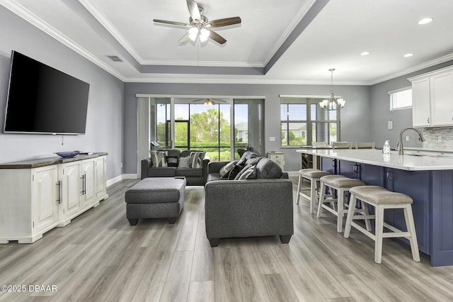 living area with visible vents, crown molding, baseboards, ceiling fan with notable chandelier, and light wood finished floors