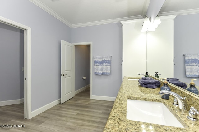bathroom featuring a sink, baseboards, crown molding, and wood finished floors