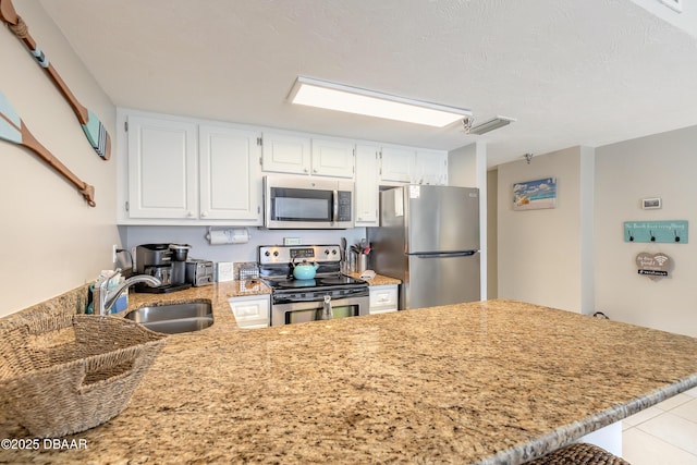 kitchen with appliances with stainless steel finishes, sink, white cabinets, light tile patterned floors, and kitchen peninsula