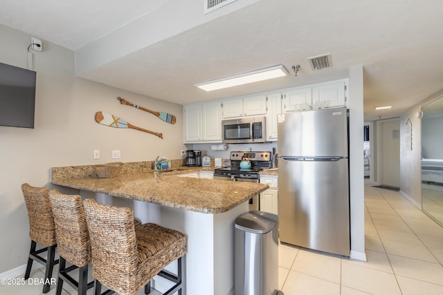 kitchen with a breakfast bar, light tile patterned floors, appliances with stainless steel finishes, kitchen peninsula, and white cabinets