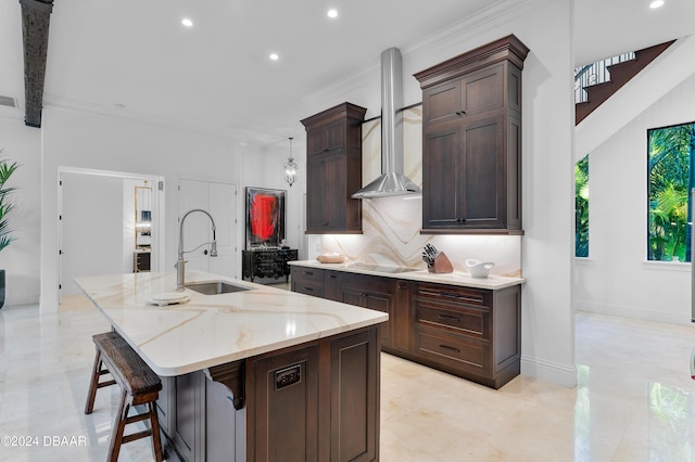 kitchen with a breakfast bar, a spacious island, sink, light stone counters, and wall chimney exhaust hood