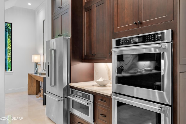 kitchen featuring light stone countertops, appliances with stainless steel finishes, dark brown cabinets, and decorative backsplash